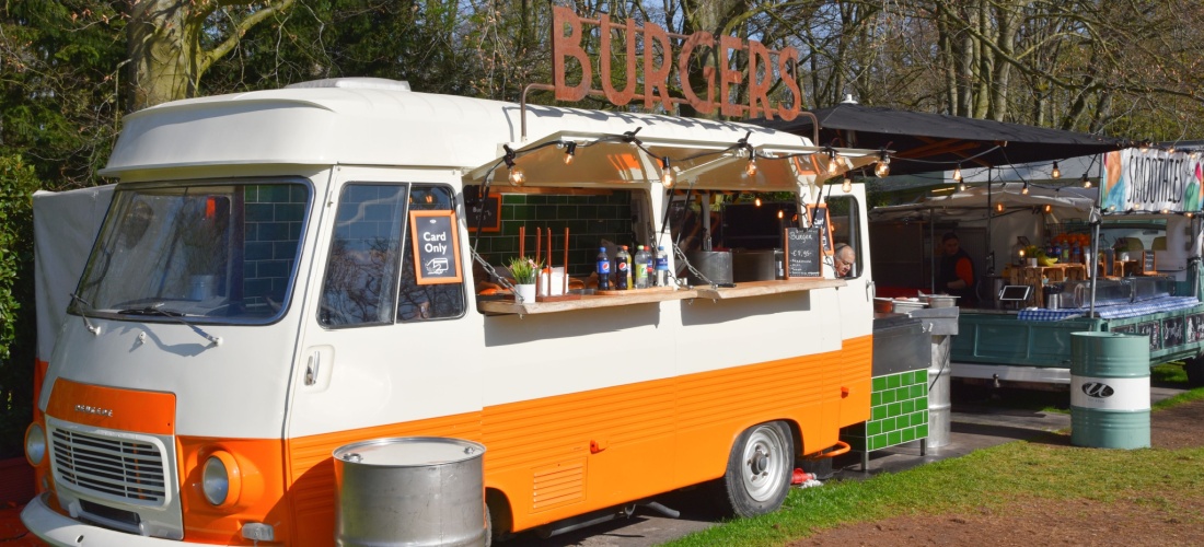 Foodtruck blanca y naranja con letrero de burguers en el techo